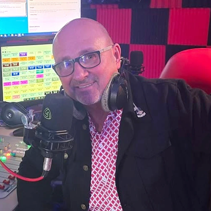Brian Ovens seated at a radio studio microphone, with headphones around his neck.